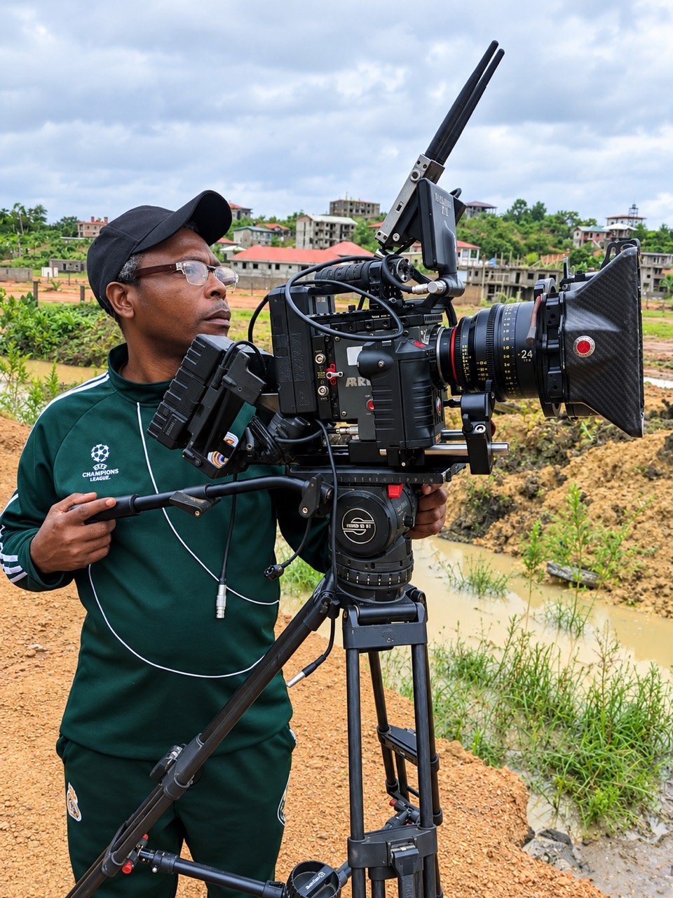 A cinematographer operating an ARRI cinema camera on a tripod outdoors.
