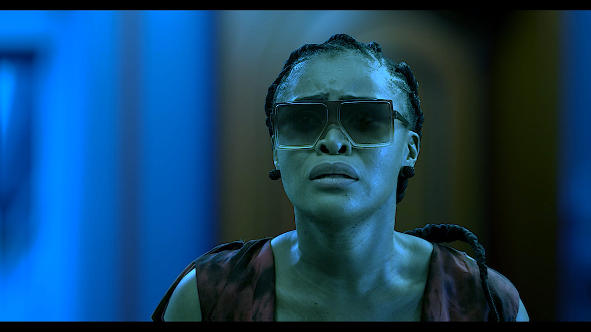 A performer wearing a wide visor, lit in deep blue on a science fiction set.