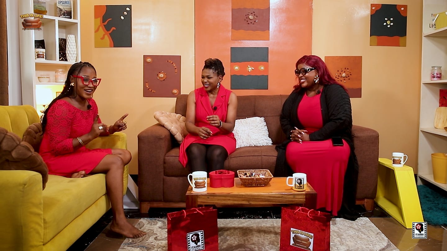 Three presenters seated together on a warmly lit talk show set.