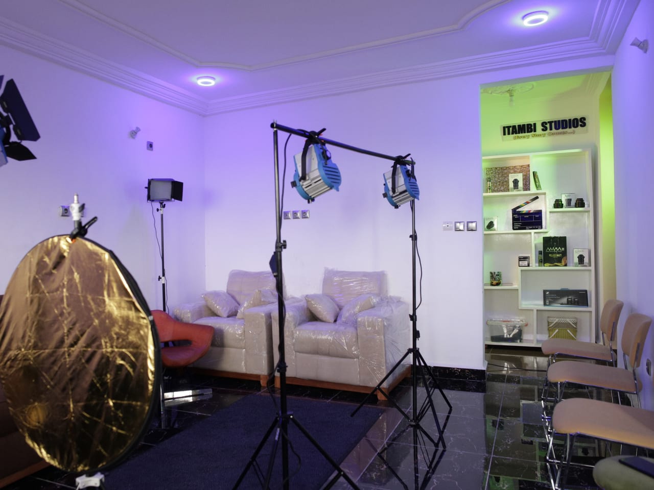 Studio lighting stands and a gold reflector beside an Itambi Studios branded shelf display.