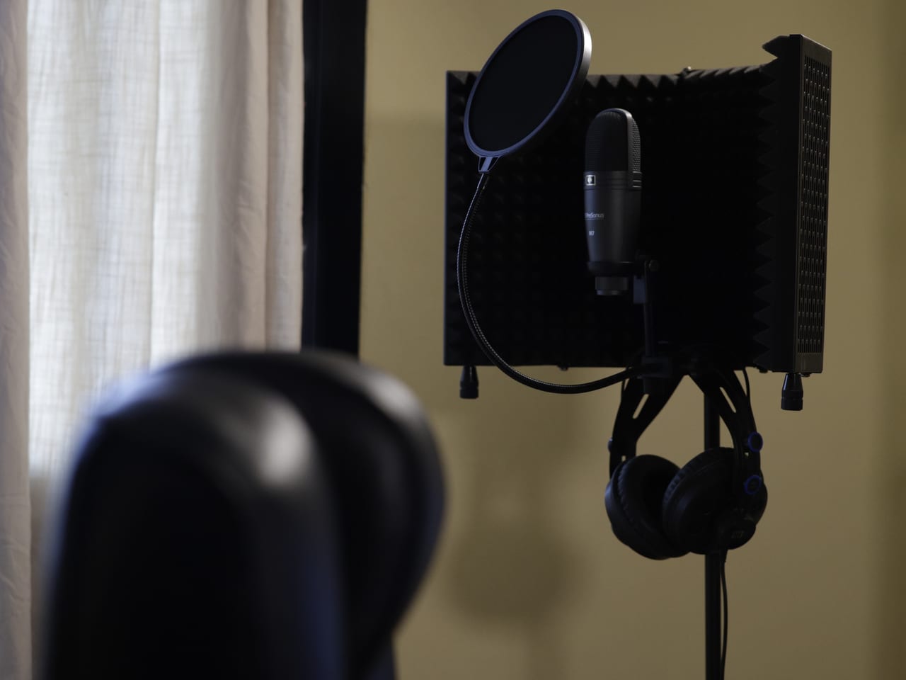Studio recording microphone with a pop filter, acoustic shield, and headphones.