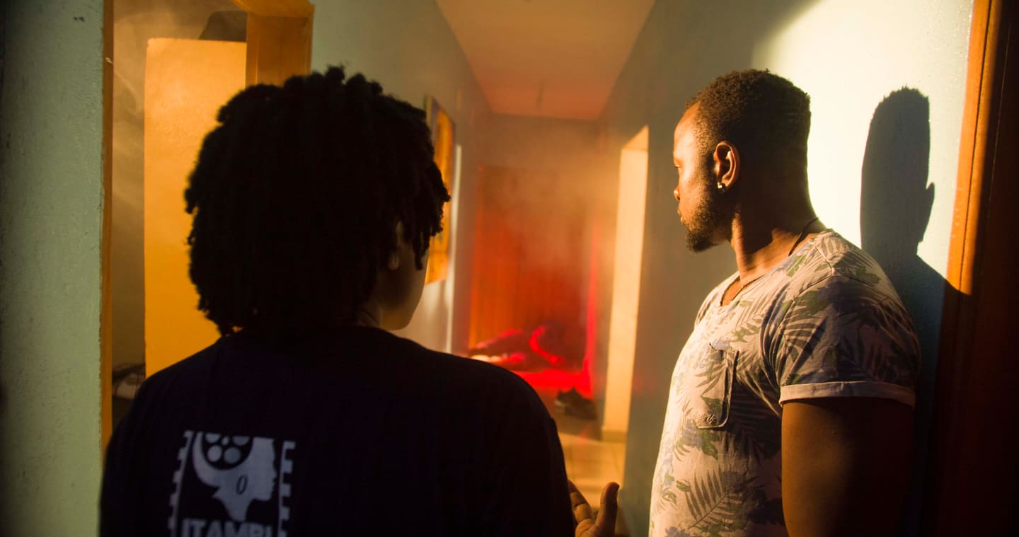 Two performers framed by warm production lighting in a doorway scene.